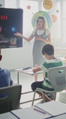 Astronomi sınıfı: Dijital Ekran kullanarak İlkokul çocuklarına Güneş Sistemi Açıklayan Kadın Öğretmen. Masalarda oturan genç kızlar ve oğlanlar, sınıfta uzay bilimi öğreniyorlar. Dikey Çekim.