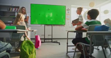 Tablet Bilgisayarlı İlkokul Çocuğu Sınıf Arkadaşlarının Önünde Sunum Yapıyor ve Öğretmen Kroma Anahtarlı Büyük Dijital Ekran Kullanıyor. Eğitim İçeriği için Yeşil Ekran Şablonu.