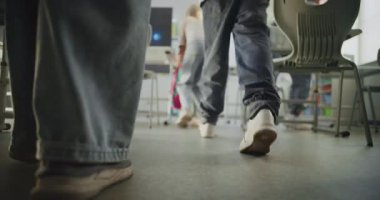 Modern Sınıfa giren ilkokul çocuklarının diz boyu çekimi, sırt çantalarını açmak ve okul malzemelerini masaya sermek. Genç Kızları ve Oğlanları Selamlayan Bayan Öğretmen. Yavaş Hareket.