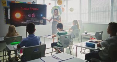 Astronomi sınıfı: Dijital Ekran kullanarak İlkokul çocuklarına Güneş Sistemi Açıklayan Kadın Öğretmen. Masalarda oturan ve Modern Sınıfta Uzay Bilimi Öğrenen Genç Kız ve Erkekler Grubu.