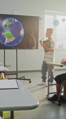 Tablet bilgisayarlı ilkokul çocuğu güneş sistemi hakkında sunum yapıyor, sınıf arkadaşlarının önündeki gezegenler ve dijital ekranı kullanan öğretmen. Akıllı Çocuklar Uzay Astronomisi okuyor. Dikey Çekim.