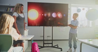 Tablet Bilgisayarlı İlkokul Çocuğu Sınıf Arkadaşları ve Öğretmen Dijital Ekran Kullanıyor 'da Güneş Sistemi ve Gezegenler Hakkında Sunum Yapıyor. Sınıfta Uzay Astronomisi okuyan Zeki Çocuklar.