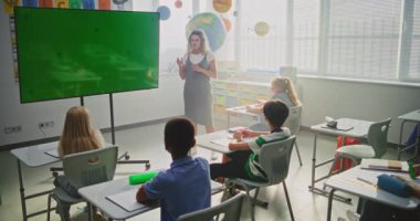 Modern Sınıflar: Chromakey Mockup ile Büyük Dijital Ekran kullanarak İlkokul Çocuklarına Öğretmenlik Yapan Kadın Sınıfı. Eğitim İçeriği veya Etkileşimli Görseller için Yeşil Ekran Yer Tutucu. Doli Vuruşu.