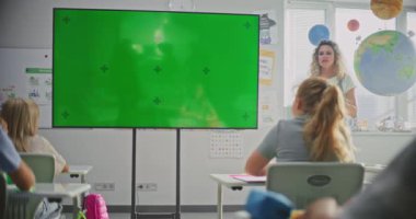 Modern Sınıfta İlkokul Öğrencilerini Eğiten Bayan Öğretmen. Büyük Dijital Ekran ve Krom Anahtar. Eğitim İçeriği veya Etkileşimli Görsel Efektler için Yeşil Ekran Şablonu