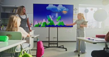 Tablet bilgisayarlı ilkokul kızı sınıfın önünde coğrafya bilgisi gösteriyor ve öğretmen dijital ekranı kullanıyor. Sınıfta Su Döngüleri ve Hava Durumu Faktörlerini Öğrenen Genç Öğrenciler.