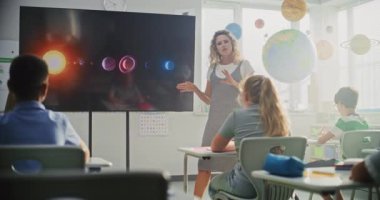 Astronomi sınıfı: Dijital Ekran kullanarak İlkokul çocuklarına Güneş Sistemi Açıklayan Kadın Öğretmen. Masalarda oturan ve Modern Sınıfta Uzay Bilimi Öğrenen Genç Kız ve Erkekler Grubu.