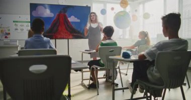 İlköğretim Okulu Öğrencileri Modern Sınıfta Jeoloji Hakkında Temel Bilgiler Çalışıyor. Sayısal Ekran Kullanımı sırasında Zeki Çocuklara Volkanik Patlama Sürecini Açıklayan Bayan Öğretmen.