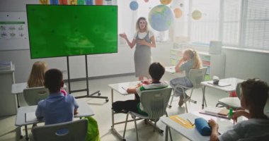 Sınıfta İlkokul Öğrencilerini Eğiten Bayan Öğretmenler. Büyük Dijital Ekran ve Krom Anahtar. Eğitim İçeriği veya Etkileşimli Görseller için Yeşil Ekran Şablonu. Doli Vuruşu.