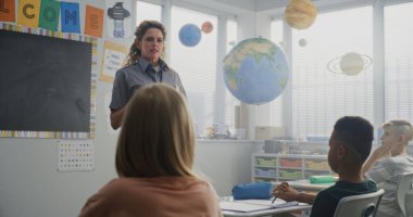 Bayan Polis Memuru Sınıfı Ziyaret Ediyor, İlkokul Öğrencilerine Güvenlik Kuralları Konusunda Ders Veriyor. Genç Çocuklar Oturuyor, Memura Özenli Dinliyor, Hukuk ve Koruma Hakkında Öğreniyor.