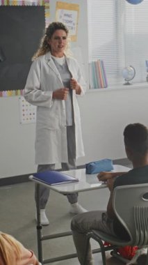 Kadın Sağlığı Profesyoneli Konuşuyor ve Genç Öğrencilere Tıp Dersi Veriyor. Çocuklar el kaldırıyor, ilkokulda sağlık ve hijyen dersi sırasında soru soruyor. Dikey Çekim.