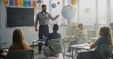 TSA Güvenlik Subayı İlköğretim Okulundaki Genç Öğrencilere Güvenlik Kurallarını Açıklıyor. Çocuklar Sorular Soruyor, Polis İşçi Rehberliğini Dinliyor Hukuk ve Sorumluluk Bilgisi Hakkında.