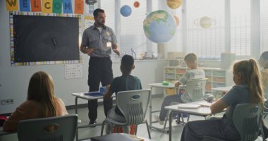 TSA Güvenlik Subayı İlköğretim Okulundaki Genç Öğrencilere Güvenlik Kurallarını Açıklıyor. Çocuklar Sorular Soruyor, Polis İşçi Rehberliğini Dinliyor Hukuk ve Sorumluluk Bilgisi Hakkında.