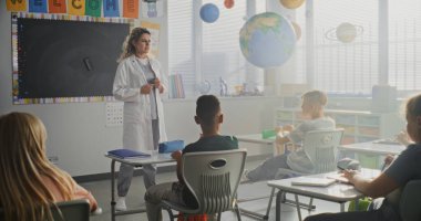 Beyaz önlüklü bayan doktor ziyaret sınıfında, İlkokul öğrencilerine sağlık ve hijyenle ilgili ders veriyor. Genç Çocuklar Oturuyor ve Dinliyor Profesyonel Sağlık Bakımına Cana Yakın.