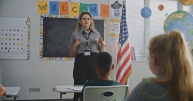 Amerikan İlköğretim Okulu 'ndaki Genç Öğrencilere Güvenlik Kurallarını Açıklayan Kadın Ulaşım Güvenlik Görevlisi. Oturan, Polis İşçilerinin Hukuk ve Sorumluluk Bilgisi Hakkında Rehberliğini Dinleyen Çocuklar.