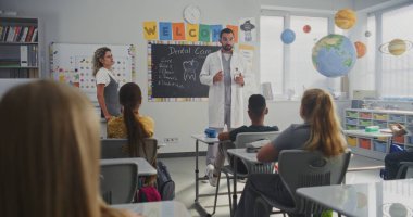 Erkek Sağlığı Profesyoneli Diş Bakımı Meraklı Genç Öğrencilere Açıklama Kuralları. Çocuklar İlköğretim Okulu 'nda Sağlık ve Hijyen Dersinde Soru Soruyor, Dişçiyi Dikkatle Dinliyor.