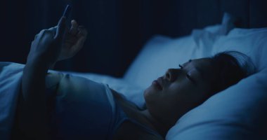Battaniyenin Altında Yatan Düşünceli Asyalı Kadın portresi, Bakışlı Telefon. Karanlık Yatak Odasında Akıllı Telefon Kullanan Uykusuz Kız. Uykusuzluk, Teknoloji Bağımlılığı, Uykudan Önce Duygular, Yalnızlık.