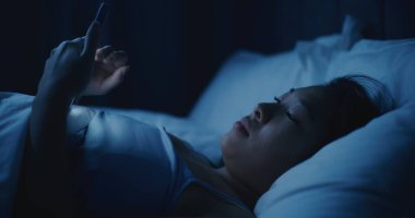 Battaniyenin Altında Yatan Düşünceli Asyalı Kadın portresi, Bakışlı Telefon. Karanlık Yatak Odasında Akıllı Telefon Kullanan Uykusuz Kız. Uykusuzluk, Teknoloji Bağımlılığı, Uykudan Önce Duygular, Yalnızlık.