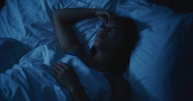 Endişeli düşünceleri olan yorgun Asyalı kadın geceleri uyuyamıyor. Kız daha rahat bir şekilde uzanmaya ve uykuya dalmaya çalışıyor. Stres kavramı, uykusuzluk, endişeli düşünceler, kötü uyku. Sabit Çekim.