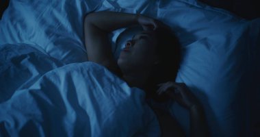 Endişeli düşünceleri olan yorgun Asyalı kadın geceleri uyuyamıyor. Kız daha rahat bir şekilde uzanmaya ve uykuya dalmaya çalışıyor. Stres kavramı, uykusuzluk, endişeli düşünceler, kötü uyku. Sabit Çekim.