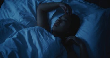 Endişeli düşünceleri olan yorgun Asyalı kadın geceleri uyuyamıyor. Kız daha rahat bir şekilde uzanmaya ve uykuya dalmaya çalışıyor. Stres kavramı, uykusuzluk, endişeli düşünceler, kötü uyku. Sabit Çekim.