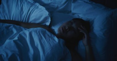 Endişeli düşünceleri olan yorgun Asyalı kadın geceleri uyuyamıyor. Kız daha rahat bir şekilde uzanmaya ve uykuya dalmaya çalışıyor. Stres kavramı, uykusuzluk, endişeli düşünceler, kötü uyku. Sabit Çekim.