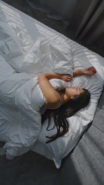 Sabah, Genç Kız Şık Yatak Odasında Rahat Bir Yatakta Uyuyor. Beyaz Yataklı Asyalı Kadın, Koyu Saçları Yastığın Üzerinde Güzel Yalan Söylüyor. Konsept Sağlıklı Uyku, Güzel Sabah Rutini. Dikey Çekim.