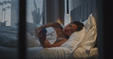 Günün Sonrası Yatağında Rahatlayan Genç Kadın. Kız Sosyal Medya Bilgileri, Mesajları ve Gülümsemeleri Kontrol Ediyor. Zor bir günün ardından rahatlama, uzaktan iletişim ve özbakım kavramını kabul et. El bilgisayarı.