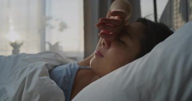 Güzel genç kadın, yumuşak battaniyenin altında rahat bir yatakta uyanıyor. Kız, güneş ışığıyla dolu yatak odasında esniyor ve gülümsüyor. Sağlıklı Uyku, Dinlenme ve Güzel Sabah Rutini kavramı. El yapımı..