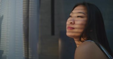 Genç Kadın Güneşli Yatak Odasında Sabah Uyanır. Kız uykulu bir gülümsemeyle yatakta oturur ve pencereden dışarı bakar, yüzüne güneş ışığı düşer. Günaydın, Pozitif Ruh hali. Rahatlama ve uyku kavramı.