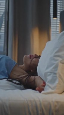 Akşamları, Mavi Pijamalı Genç Kadın Yatakta Yatıyor. Kız ışığı kapatır, yastığa sarılır, uykuya dalar. Kavram, zor bir günün ardından rahatlama, sağlıklı uyku ve iyileşme, kişisel bakım. Dikey Çekim.