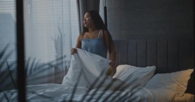 Şık Yatak Odası 'ndaki Uzun Saçlı Asyalı Kız Yatakta Rahat Uzanıyor, Üstünden Battaniyeyi Çekiyor ve Smartphone' da Çevrimiçi Hayata Batıyor. Sabah Rutini kavramı, Dijital Yaşam Tarzı. El bilgisayarı.