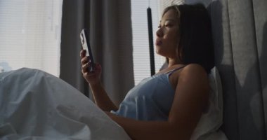 Uzun Koyu Saçlı Güzel Asyalı Kadınların Giyinmesi Akıllı Telefon ve Gülücüklerle Haber Kaynağı Arasında Oturması. Kavram Sabah Rutini, Sosyal Yaşam, Dijital Yaşam Tarzı. El bilgisayarı.