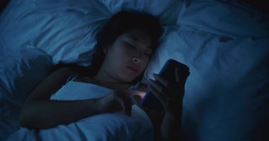 Genç Kadın Karanlık Yatak Odasında, Battaniyenin Altında Yatıyor, Akıllı Telefona Odaklandı. Düşük Işıkta Telefonlu Kız 'ın Yatma Vakti Portresi. Gece Tarayıcılığı, Uykusuzluk, Teknoloji ve Özel Duygular kavramı.