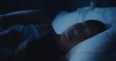 Battaniyenin Altında Yatan Düşünceli Asyalı Kadın portresi, Bakışlı Telefon. Karanlık Yatak Odasında Akıllı Telefon Kullanan Uykusuz Kız. Uykusuzluk, Teknoloji Bağımlılığı, Uykudan Önce Duygular, Yalnızlık.