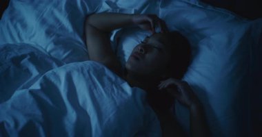 Endişeli düşünceleri olan yorgun Asyalı kadın geceleri uyuyamıyor. Kız daha rahat bir şekilde uzanmaya ve uykuya dalmaya çalışıyor. Stres kavramı, uykusuzluk, endişeli düşünceler, kötü uyku. Sabit Çekim.