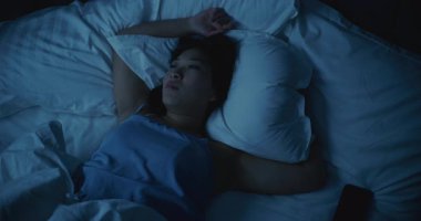 Uykusuzluk çeken, yatakta huzursuz ve huzursuz Asyalı bir kız. Uykuya dalmak için çırpınıyor, dönüyor ve mücadele ediyor. Yüzünde stres, endişe ve yorgunluk belirtileri var. Yoksul Dinlenme, Gerilim, Uykusuzluk Konsepti.