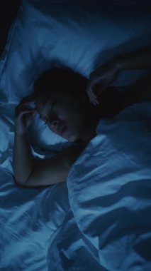 Endişeli düşünceleri olan yorgun Asyalı kadın geceleri uyuyamıyor. Kız daha rahat bir şekilde uzanmaya ve uykuya dalmaya çalışıyor. Stres kavramı, uykusuzluk, endişeli düşünceler, kötü uyku. Dikey Çekim.