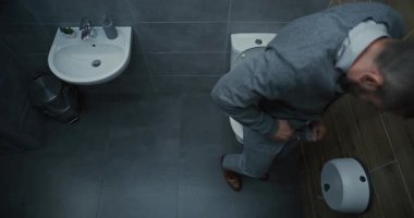 Pantolonunu çıkaran, tuvalette oturan, ishal ve mide ağrısından muzdarip bir adam. Modern Ofiste Çalışırken İşadamı Sindirim Rahatsızlığı ve Hazımsızlık Yaşıyor. Yüksek Açı.