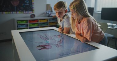 Sınıfta Dokunmatik Ekran Masası 'nda Çocuklar Kas Sistemi Üzerinde Çalışır. Öğrenciler İletişim Kurar, Fikirleri Paylaşır, 3D Anatomi Modelini Birlikte Keşfeder. İnteraktif Öğrenme kavramı, BTMM Eğitimi. Doli Vuruşu.