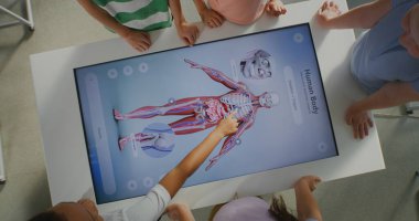 Okul Sınıfı 'ndaki Etkileşimli Dokunmatik Ekran' ın yakın çekimi. Genç Öğrenciler Modern Dokunmatik Ekran 'ın etrafında toplanarak Kas Sistemi' ni İncelemeye başladılar. Dijital Eğitim. Üst Görünüm Döndürülüyor.