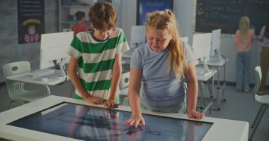 Dijital Dokunmatik Masa Masasında Gözlüklü ve Sarışın Kız, Kas ve Doku Çalışmaları Yapıyor. Bilgisayar ve Sınıf Arkadaşlarıyla Parlak Sınıflar Ortamı. STEM Eğitim kavramı.
