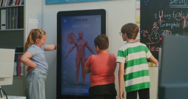 Çocuklar İnteraktif Ekranda Anatomiyi Keşfeder. Modern Dijital Sınıfta 3 Boyutlu Model Vücutla Çarpışan Üç Öğrenci. Kavram Bilimi Eğitimi, Biyoloji Öğrenimi, Etkileşimli Teknoloji. El bilgisayarı.