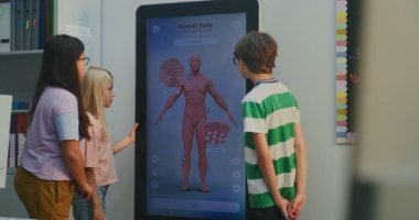 Çocuklar insan vücudunu interaktif ekranda inceliyor. Modern Sınıfta İki Kız ve Erkek, İnsan Vücudunun 3 Boyutlu Modelini Gösteren Büyük Dijital Ekranla Etkileşiyor. Doğal Bilimler Anatomisi Etkileşimli Çalışması.