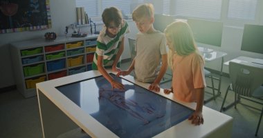 Bir grup öğrenci insan vücudunun 3 boyutlu modeliyle etkileşimli dijital masa etrafında toplandı. Okul Çocukları Anatomiyi Göster ve Tartış. Konsept Takım Çalışması, Biyoloji Dersleri ve Dijital Eğitim. Doli Vuruşu.