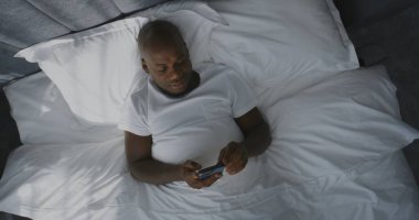 Yetişkin Adam, Smartphone Haber Kaynağını Sabah Yatağında Geçiriyor. Gülümseyen Afrikalı Amerikalı Adam Sosyal Medyadan İçerik Bakıyor. Concept Connected Lifestyle, Morning Digital Routine. Üst Görünüm Döndürülüyor.