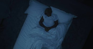 Geceleri, yataktaki adam huzursuz rüyalar görür. Pamuk Prenses 'in üstünde Afro-Afrikalı Yetişkin Adam Yatakta Dönüyor. Kâbuslar, Kötü Uyku ve Zor Günlerden Sonra Yorgunluk kavramı. Üst Görünüm Döndürülüyor.