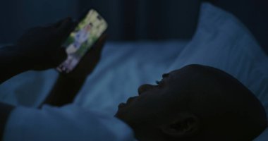 Gece, Sim Light Altında Adam Yatıyor ve Smartphone 'da Sosyal Medya aracılığıyla bitmek bilmeyen parşömenler. Sağlıksız uyku alışkanlıkları, Dijital bağımlılık, Uykusuzluk, Stres ve Uykusuzluk kavramı. Sabit Çekim.