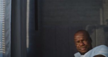 Yatak odasında, Uykucu Afrikalı Amerikalı Adam Sıcak Güneş Işığıyla Yatağında Oturuyor. Adam Pozitif Ruh hali içinde uyanıyor ve Pencereden Rüya Gibi Bakıyor. Sağlıklı Uyku, Pozitif Duygular, Rahatlama kavramı. Portre.