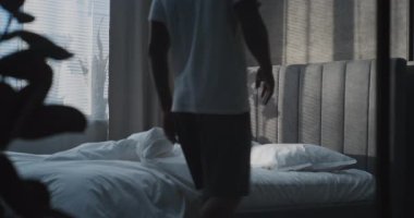 Modern, Şık Yatak Odası 'nda, Yetişkin Adam, Yumuşak Beyaz Battaniyenin Altında Yatıyor, Rahatlıyor ve Uyumaya Hazırlanıyor. Rahatlık, Konforlu Dinlenme, Yaşam Tarzı, Ev İçi ve Rahatlama Konsepti. Sabit Çekim.