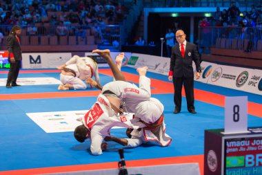 ABU DHABI, UAE - 19 Nisan 2016: ABU DHABI World PROFESSIAL JIU-JITSU CHAMPIONSIP 2016, IPIC ARENA. Kahverengi kemerli dövüşçüler saldırganca dövüşürler. Hakem onları takip ediyor..